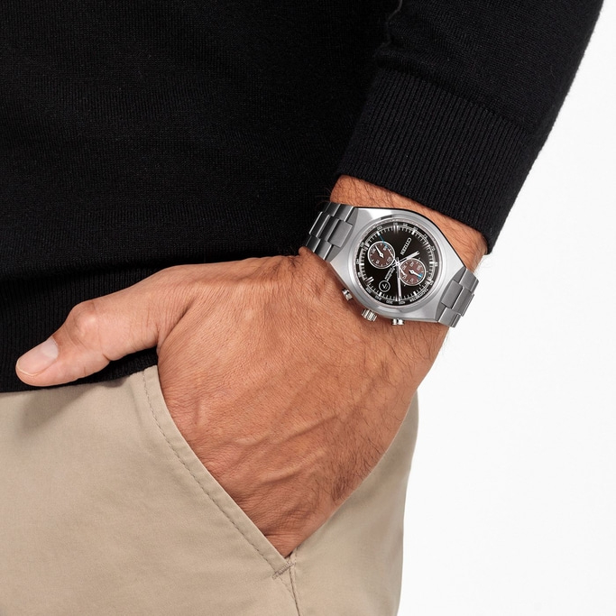 Mann mit Citizen-Uhr, schwarzem Pullover und khakifarbener Hose mit Hand in der Tasche.