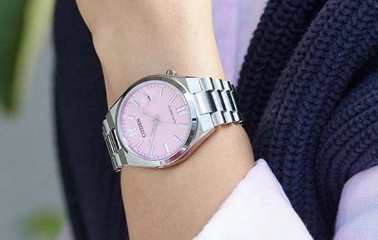 Eine Nahaufnahme einer Person, die eine silberne Citizen-Uhr mit einem pinken Zifferblatt trägt.