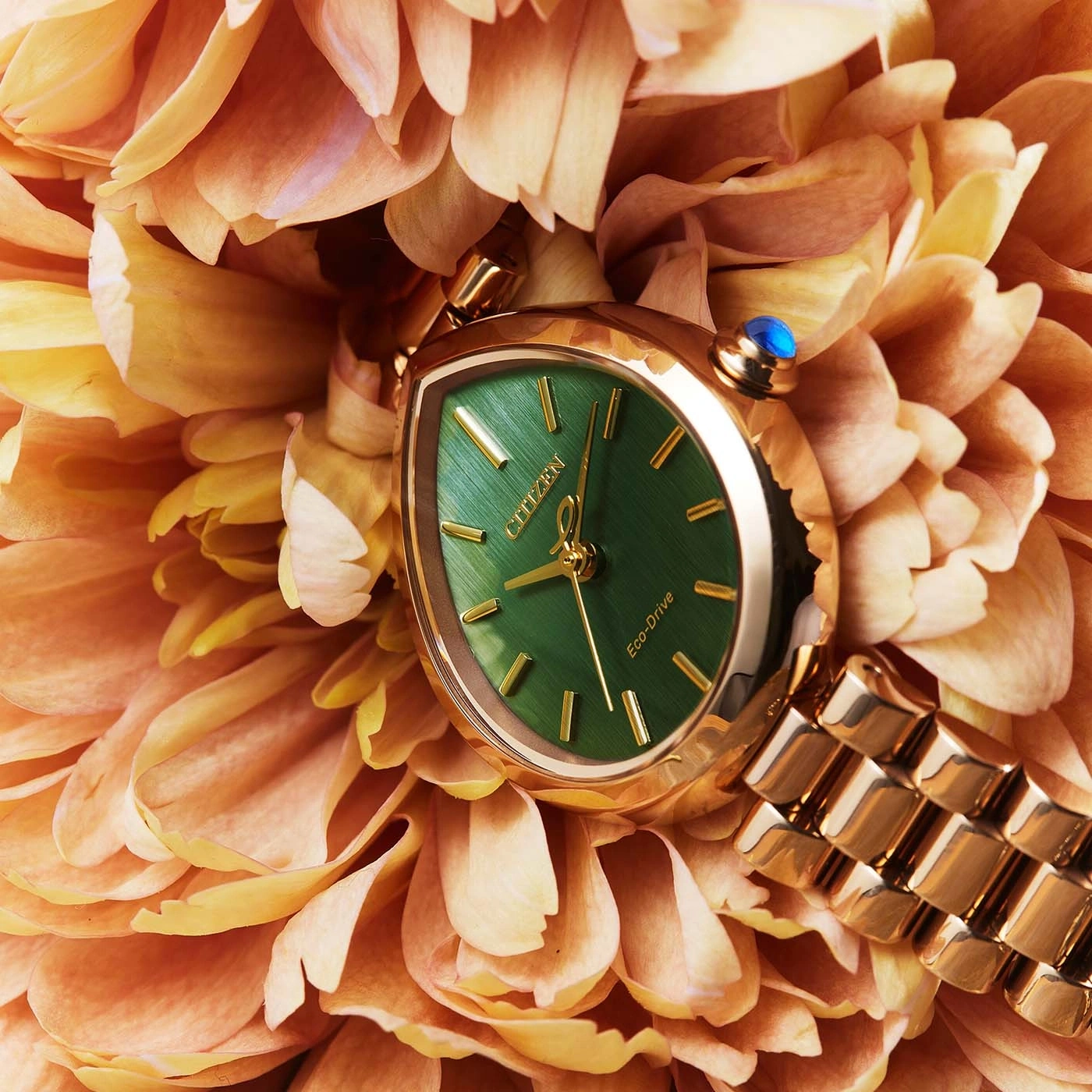 Eine goldene Uhr mit grünem Zifferblatt ruht auf orangefarbenen Blütenblättern.