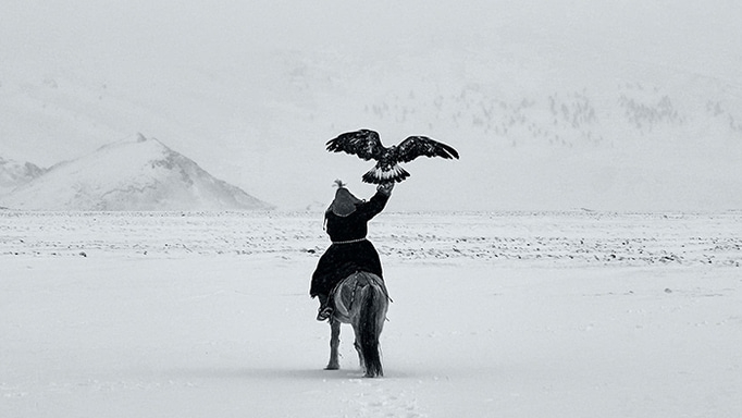 Reiter in verschneiter Steppe hält einen Adler in die Luft – kraftvoll und still.