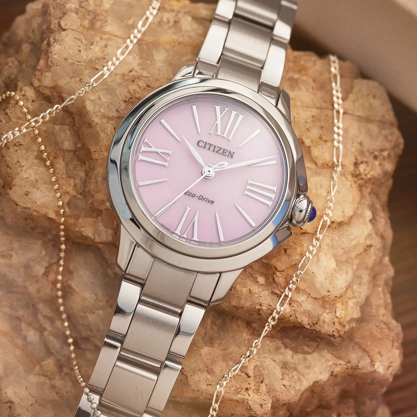 Citizen-Uhr mit rosa Zifferblatt und silbernem Armband, mit einer Halskette.