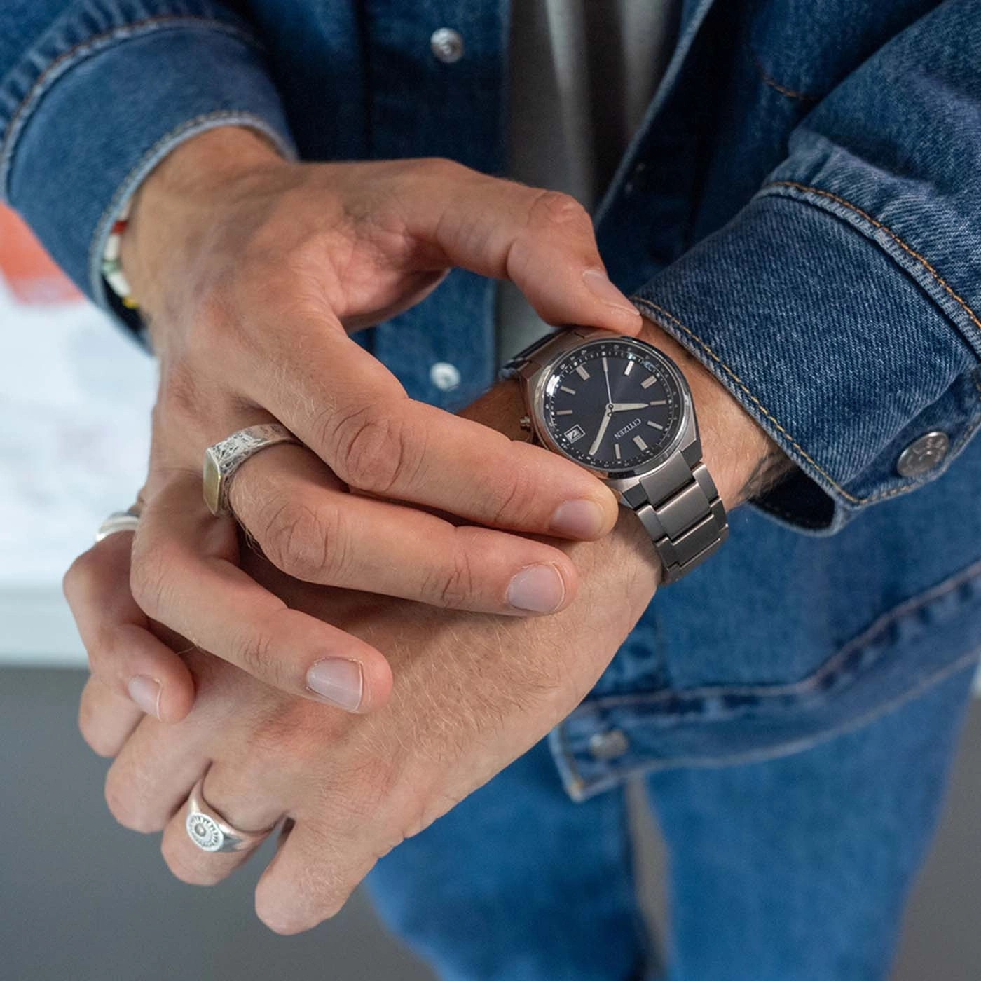 Mann überprüft seine Uhr, trägt eine Jeansjacke und Ringe.