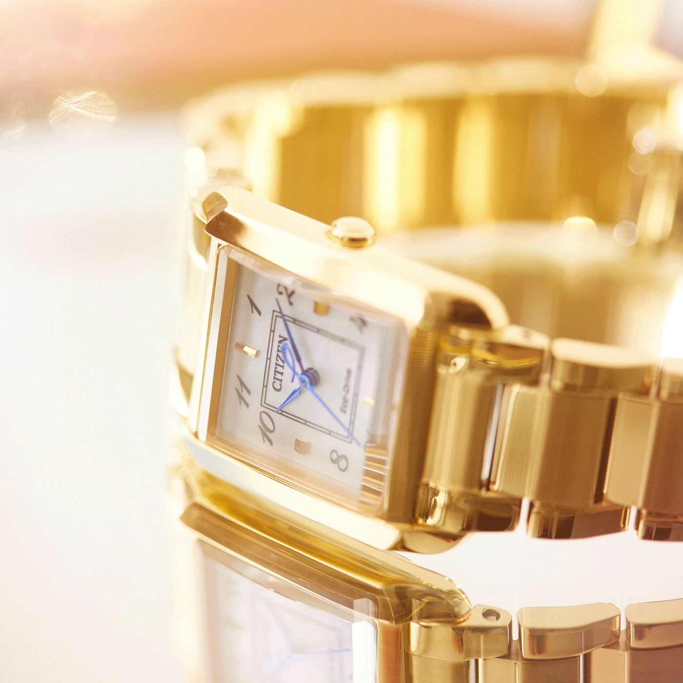 Nahaufnahme einer goldenen Citizen-Uhr mit rechteckigem Zifferblatt und blauen Zeigern.
