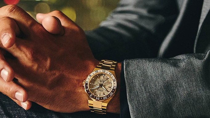 Mann trägt eine goldene Uhr mit strukturiertem Zifferblatt und goldenem Armband.
