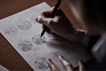 This image shows an overhead view of hands sketching intricate watch movement designs on paper. Several circular diagrams detail gears and components, highlighting the precise and artistic process of watchmaking design.