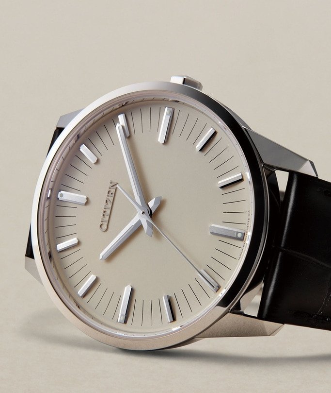 This close-up features a Citizen watch with a clean, light-toned dial and a polished silver-toned case, paired with a dark leather strap. It showcases slender hands and prominent applied hour markers, emphasizing its minimalist and elegant design on a ne