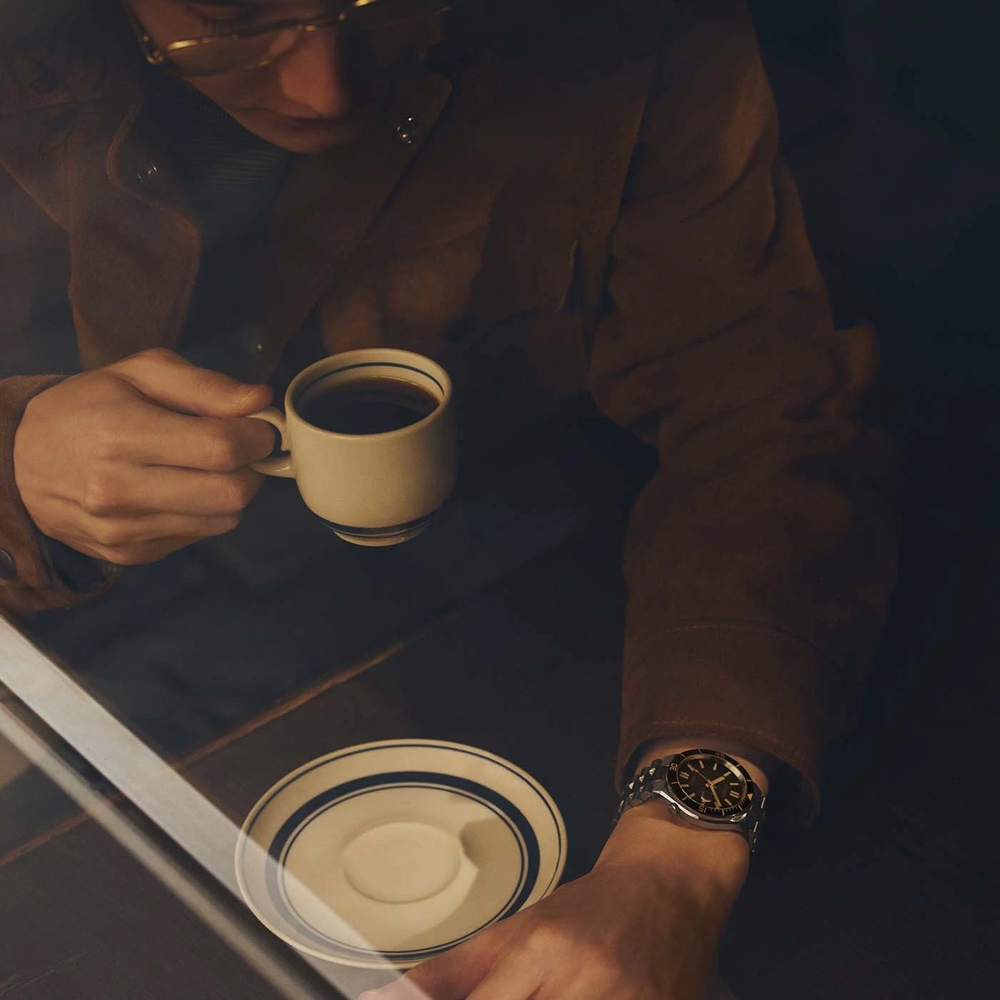 Mann in brauner Jacke trinkt Kaffee und trägt eine Uhr.